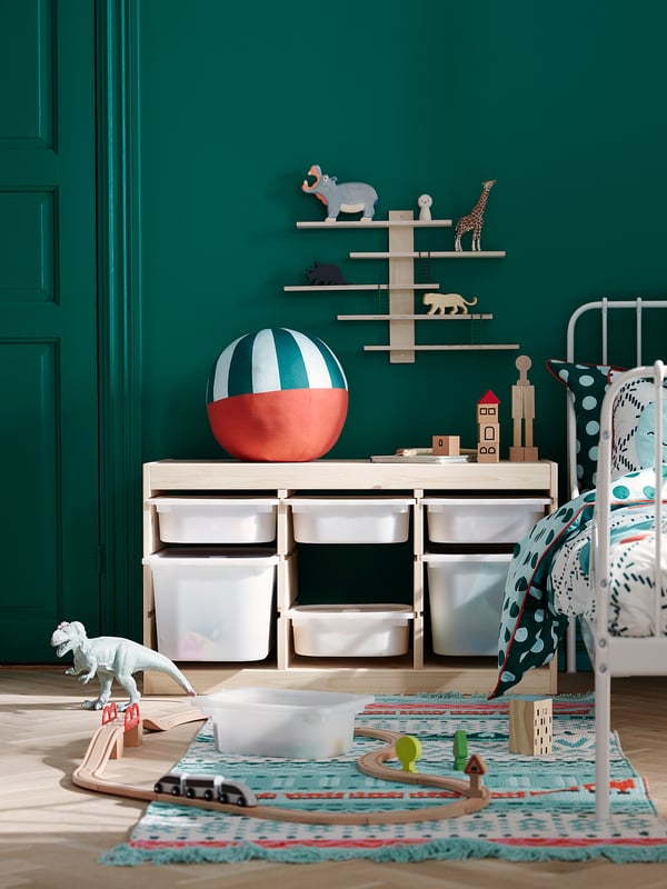 Childs playroom with green walls, white furniture, wooden toys, colorful rug, and a dinosaur figure.