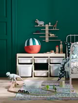 Childs playroom with green walls, white furniture, wooden toys, colorful rug, and a dinosaur figure.
