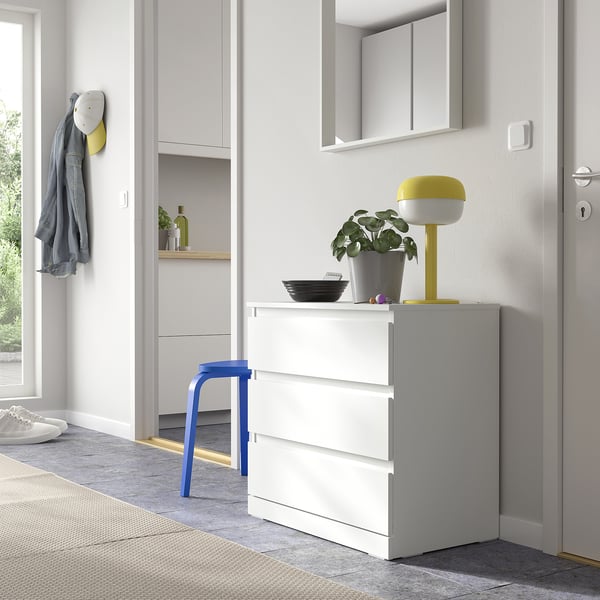 Bright yellow LILLBERGET lamp on white dresser with drawers, next to blue chair, near entrance with coat hook and door.