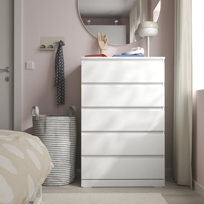 White LILLBERGET chest with 5 drawers near bed, striped laundry basket, gold decor, round lamp.
