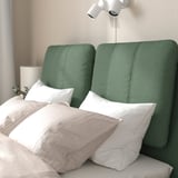 Green upholstered bed with white pillows and a wall-mounted light.