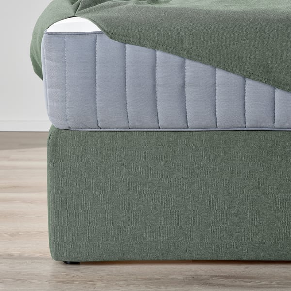 Close-up of a dark green and gray divan bed with cushions and storage under the bed.