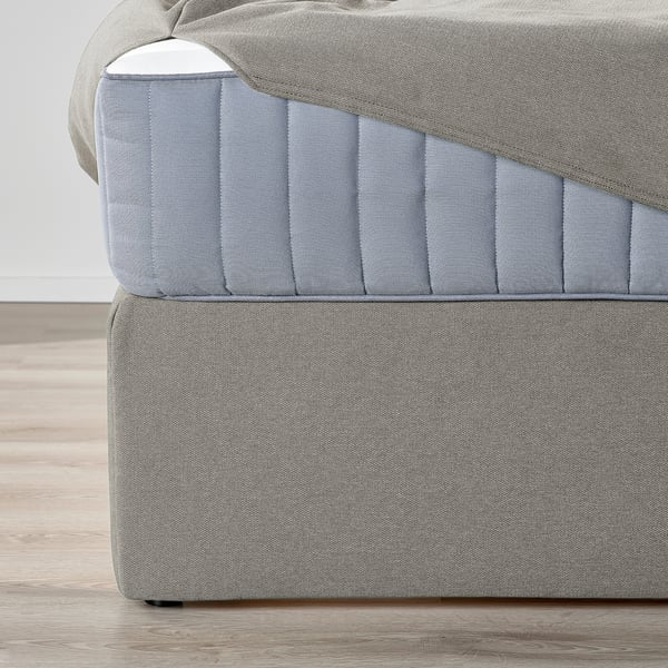 Close-up of grey fabric divan bed, showing textured cushions and sturdy upholstered sides.