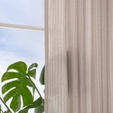 Beige and white dotted curtains hang by a window, allowing daylight while providing privacy. A green plant is in the foreground.