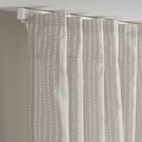 Curtains with a beige-white dot pattern hang from a white track rail, allowing light through while providing privacy.