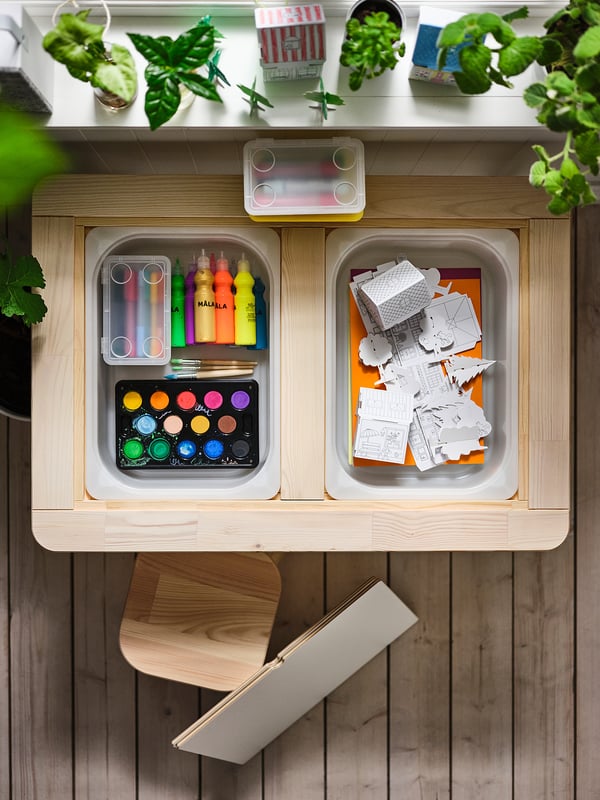 Wooden art supply drawers with colorful items and hanging plants.