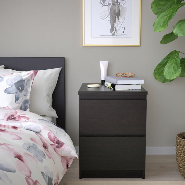 Modern bedroom with MALM nightstand, books, snacks, glass. Floral bedding, dark headboard, wall plant, picture.