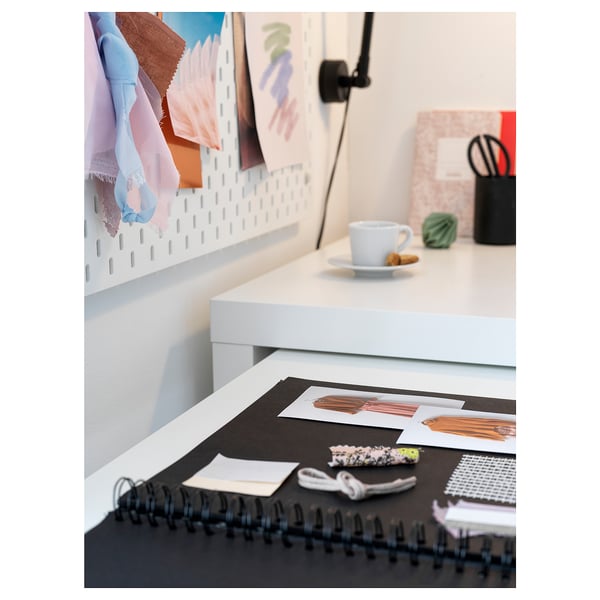 This image shows a white MALM desk with a pull-out work surface and a spiral-bound notebook on top.