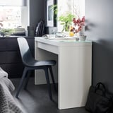 Modern black chair beside a white desk with glass top, featuring a neatly arranged workspace with decor and books in a stylish room setting.