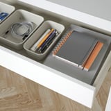 Organized desk drawer with pens, a notebook, and a charging cord in compartments.