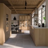 Modern kitchen with light oak cabinets, black chairs, and large window. Wooden ceiling, stainless appliances, and glass display unit.