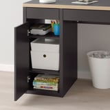 Black desk with open cabinet showing storage boxes, books, and supplies.