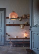 Rustic entryway: woven hats, wicker lamps, blue doors, hanging light, wall decor.