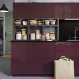 Kitchen with maroon MITTLED cabinets, glass jars with food items, and paper bag on floor.