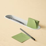 Desk organizer with pen slots, holding green sticky notes and pen. Efficient office accessory.