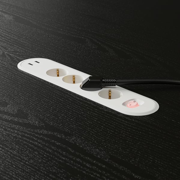 White surge protector with 3 outlets, 2 usb ports on black desk.