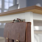 Brown leather bag hangs on metal hook under wooden ledge.