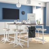 Modern office with MITTZON walnut table, stools, laptops, and water bottles. Blue walls, tv, backpack.