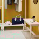 A room divider with a clothes rail, shelf, and wheels. It holds bags, helmets, and has a table surface with items.