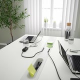 Modern office desk with integrated compartments. Three laptops, water bottles, and plants. Clean, organized workspace.
