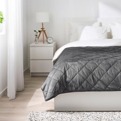 Minimalist bedroom with white walls, grey bed, & small nightstand.