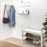 Minimalist entryway with shoe rack, coat hanger, and white shelf with decor, green plant, and beige rug.
