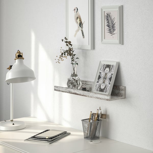 A wall shelf with rustic design displays framed art and a floral picture, holding a small vase with twigs, promoting a cozy, homely feel.