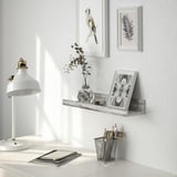 A wall shelf with rustic design displays framed art and a floral picture, holding a small vase with twigs, promoting a cozy, homely feel.