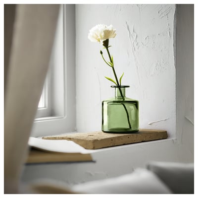 Single white carnation in a square green recycled glass vase on a window sill.