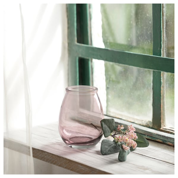 Purple recycled glass vase on wooden window sill, holding pink flowers, next to green leaves.