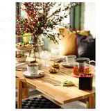 A cozy wooden table set with tea cups and treats, featuring a glass teapot and gold accents, surrounded by chairs.