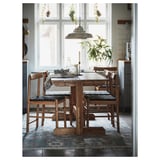 Rustic wooden dining set with acacia table and 4 woven chairs near large window; cozy decor with plants and natural textiles.