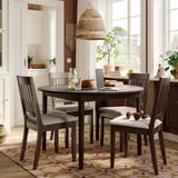 Dark wood NÄSINGE round dining set with cushioned chairs on patterned rug, large windows, cozy atmosphere.