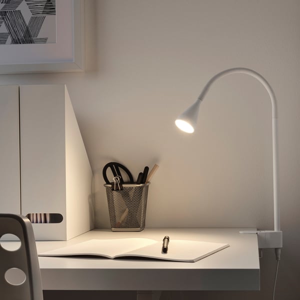 Silver NÄVLINGE lamp clamped on desk with pen holder and book.