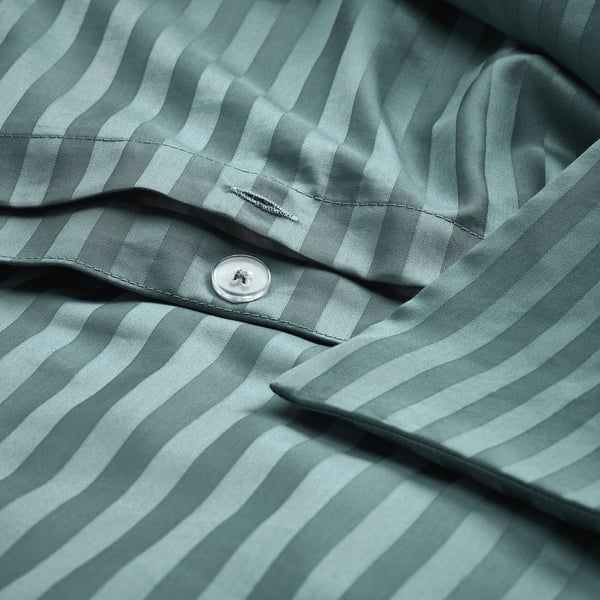 A close-up of a button on a green striped duvet cover, showcasing its smooth, lustrous sateen weave and moisture-absorbing fabric.