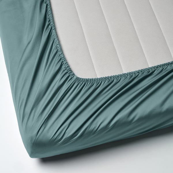 A fitted bedsheet in blue-green, made of cotton and lyocell. It elastic edges to fit mattresses up to 26 cm thick.