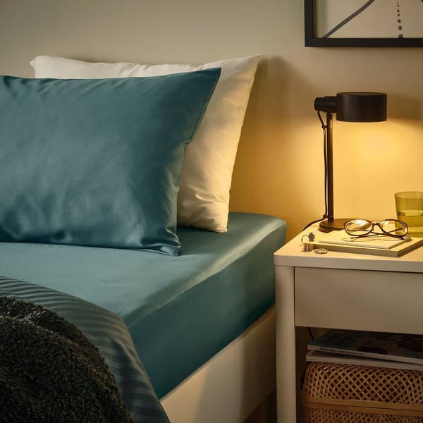 Cozy bedroom corner with teal bedding, nightstand, lamp, and decor.