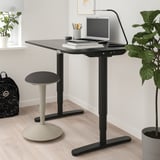 Black NILSERIK standing stool with padded seat, between plants, compact for small spaces.