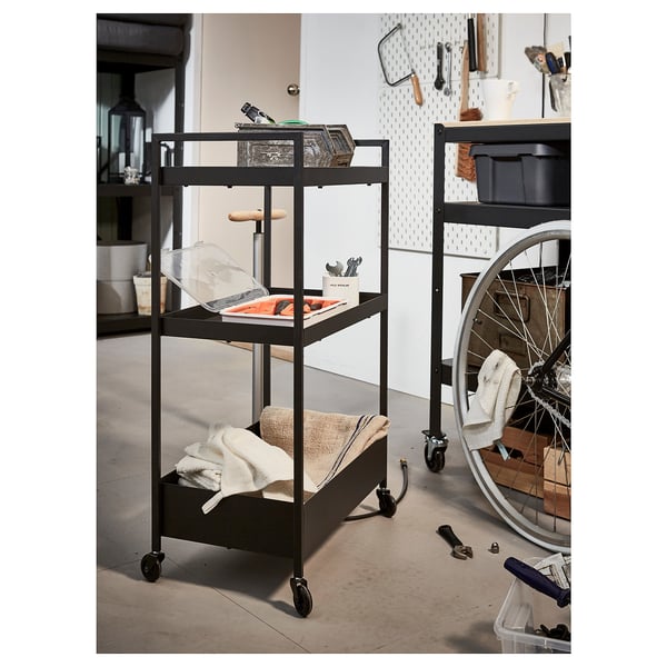 Black rolling storage cart with three shelves, featuring tools, towels, and boxes; ideal for garage or workshop organization.