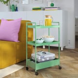 Green NISSAFORS trolley under couch, holding juice, popcorn, game controller, and board games.