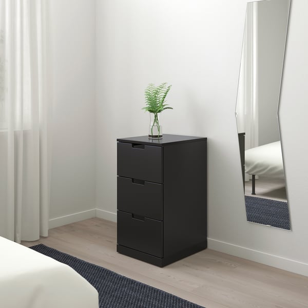 Black NORDLI 3-drawer chest, plant, mirror, bed, rug.