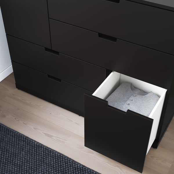 Black chest of drawers with one drawer open, revealing folded gray clothing. Drawers have smooth, soft-close mechanisms.