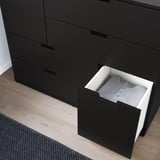 Black chest of drawers with one drawer open, revealing folded gray clothing. Drawers have smooth, soft-close mechanisms.