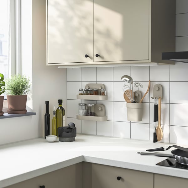 Modern kitchen with white tiles; small grey-beige wall organizers hold utensils and bottles, blending seamlessly into serene decor.
