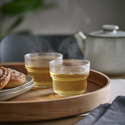 Two glasses of tea on wooden tray, steaming, with a teapot.
