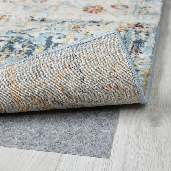 A close-up of a rolled blue patterned rug showcasing its durable, textured pile on a wooden floor.