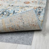 A close-up of a rolled blue patterned rug showcasing its durable, textured pile on a wooden floor.