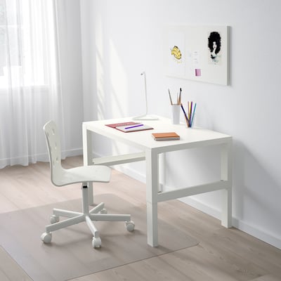 A small white adjustable desk with wheels, a chair, and colorful school supplies, positioned under a window with light curtains.