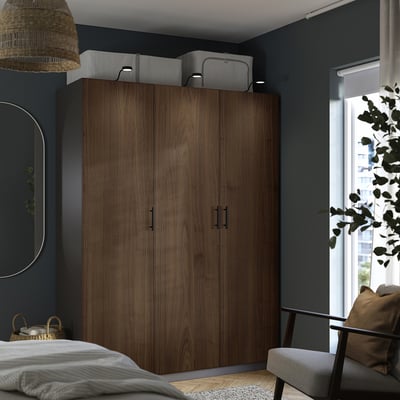 Modern bedroom with dark PAX wardrobe, large bins, circular mirror, woven pendant light, white bed, gray chair.