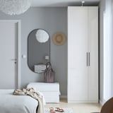 Minimalist bedroom with white PAX wardrobe, mirror, and dresser, lamp, light colors.